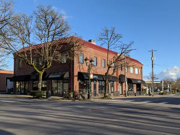 A red brick building with black awnings on a tree-lined corner in downtown Camas, Washington
